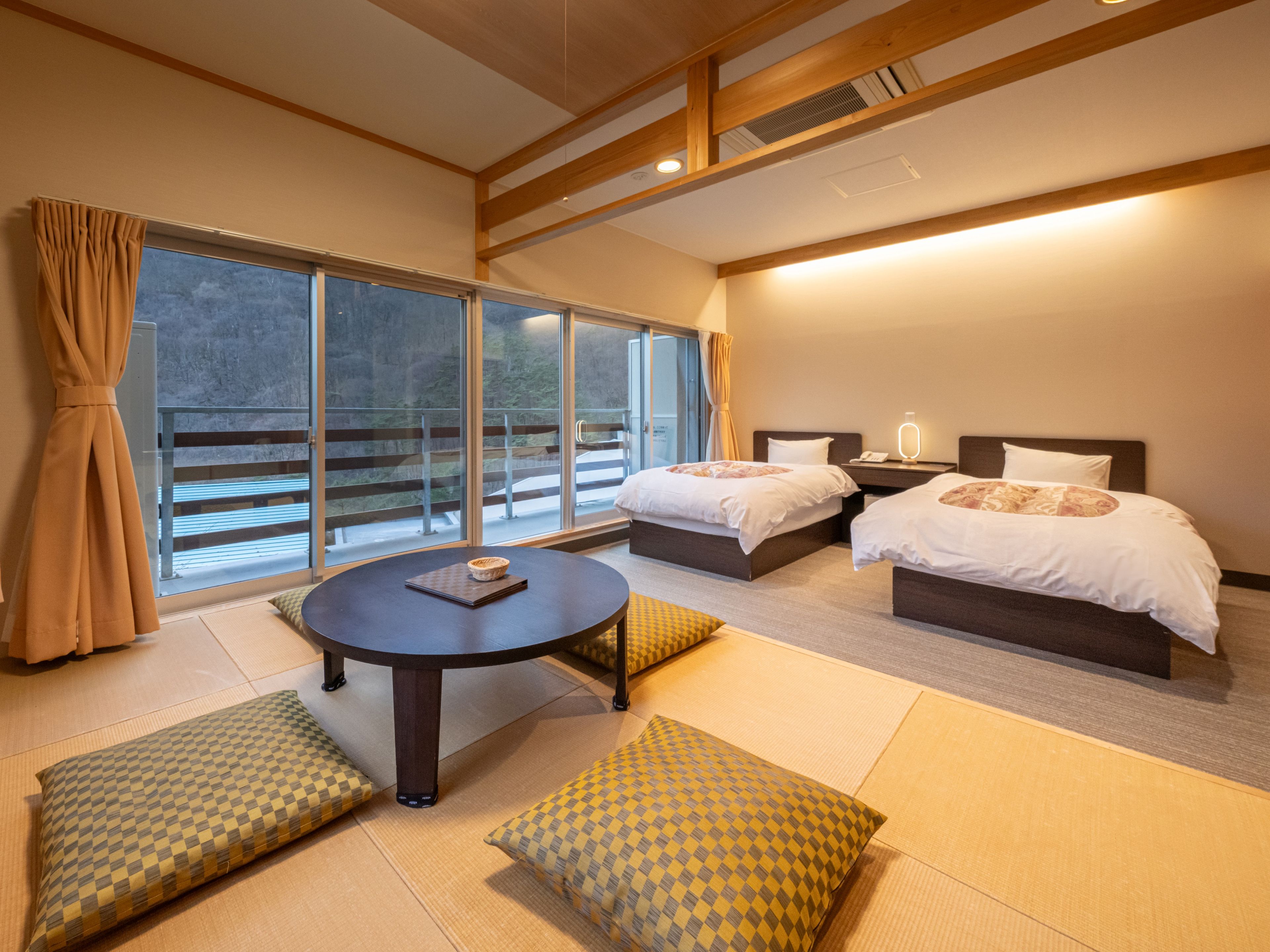A hotel room with two beds, a small table, and a view of a balcony.