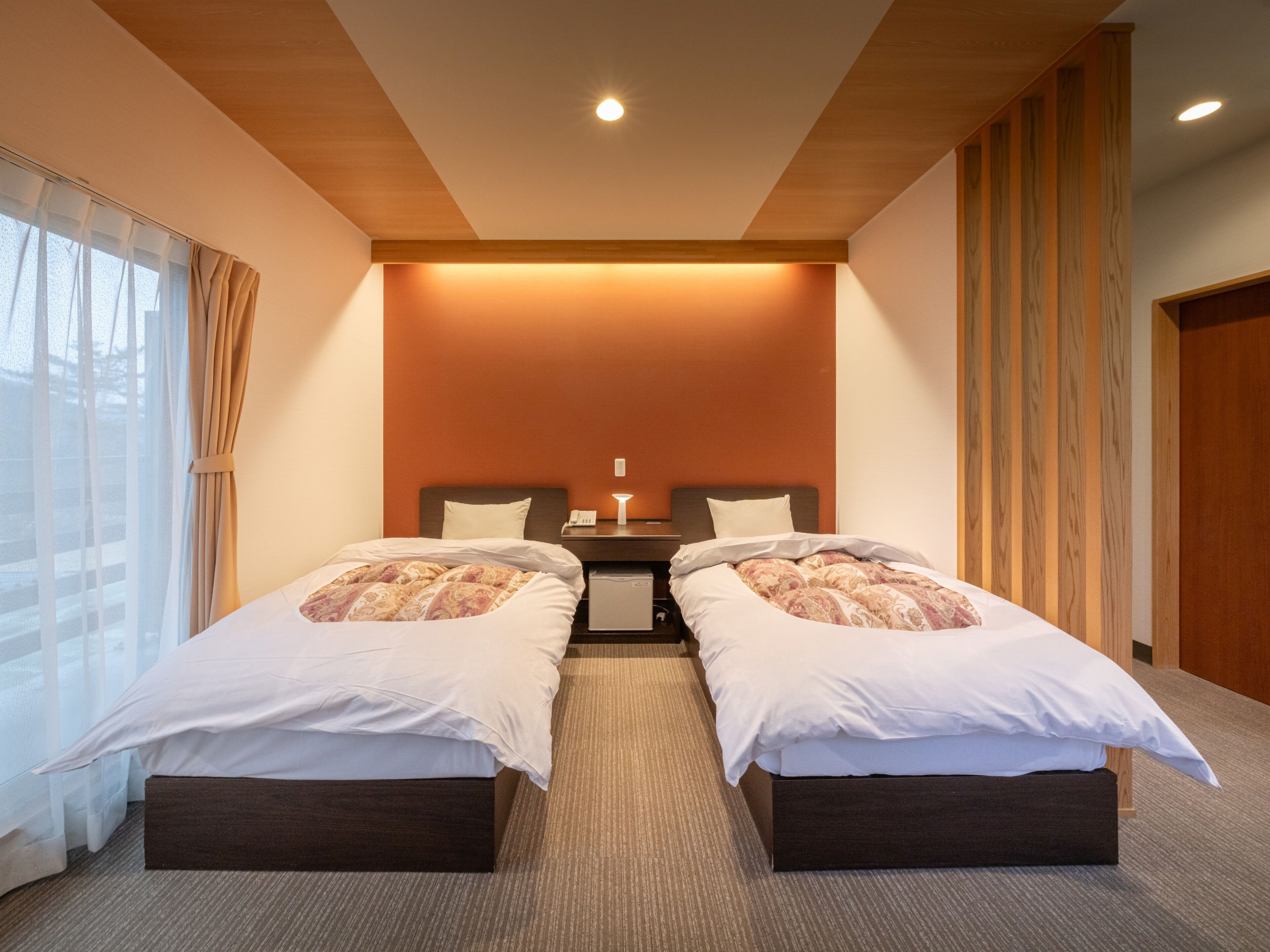 A hotel room with two beds, a wooden ceiling, and a large window with curtains.