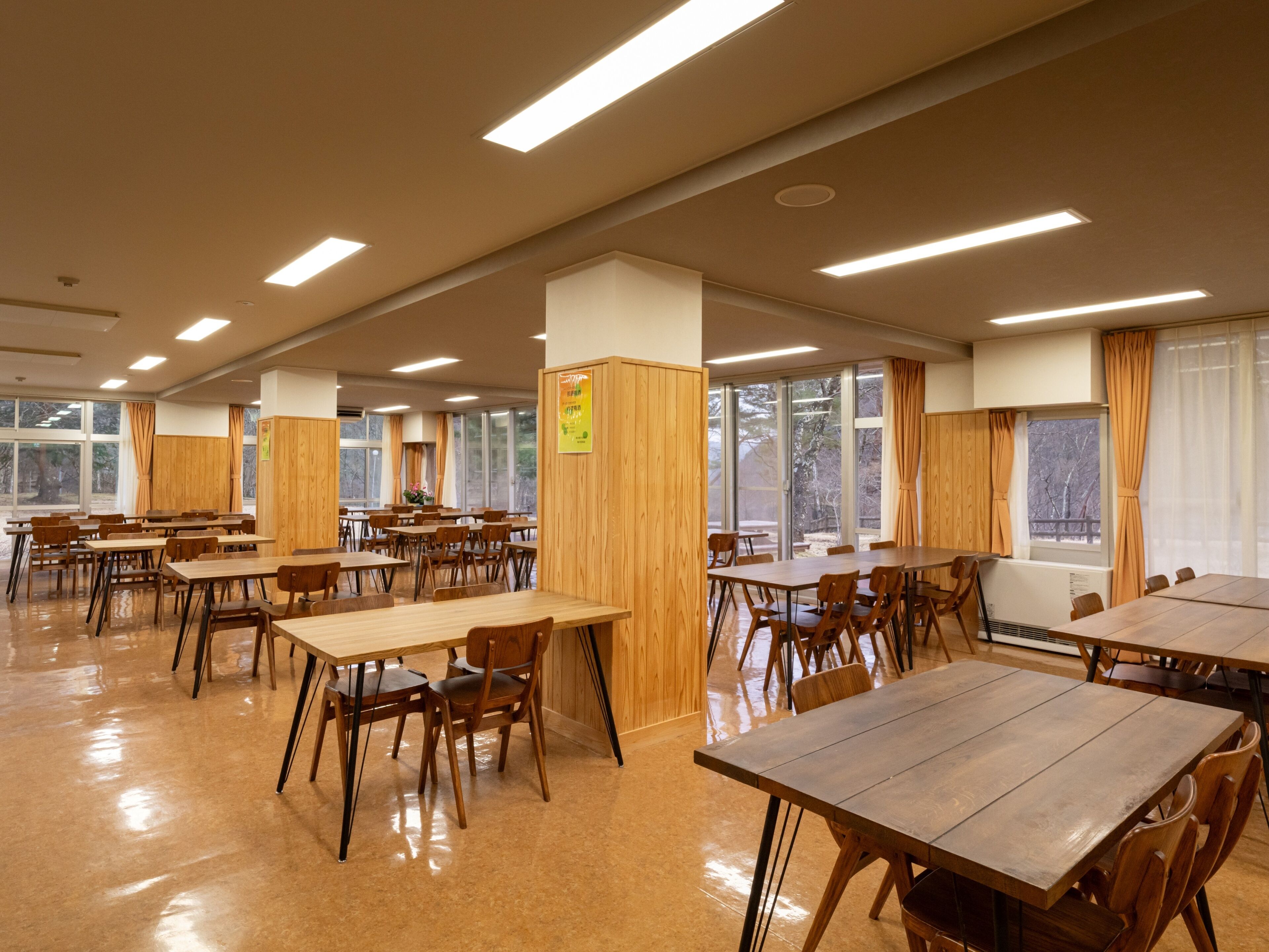 Un comedor amplio con varias mesas y sillas de madera, ventanas grandes con cortinas y un interior limpio y bien iluminado.