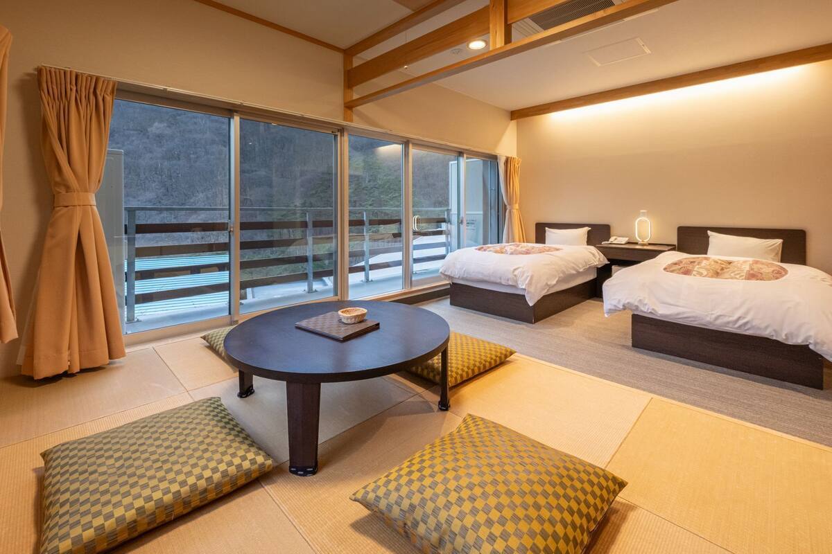 Habitación de hotel con dos camas, una mesa redonda y vistas al exterior.