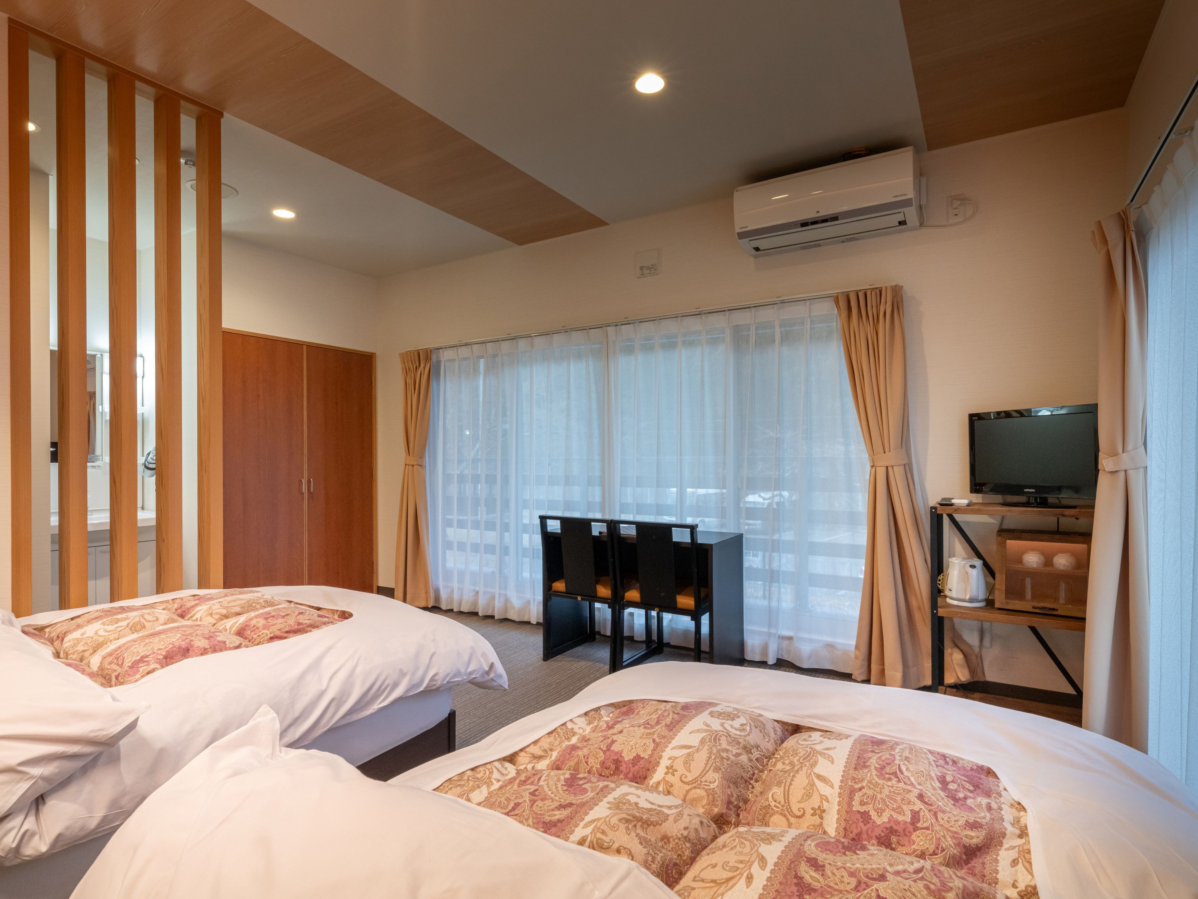 Une chambre d’hôtel avec deux lits, un bureau avec une télévision, un appareil de climatisation et une vue dégagée à travers des rideaux légers.