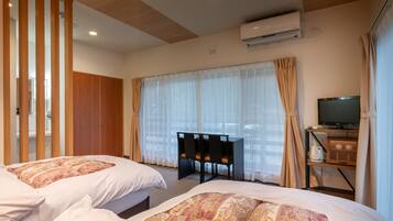 A hotel room with two beds, a desk with a television, an air conditioning unit, and a view through sheer curtains.