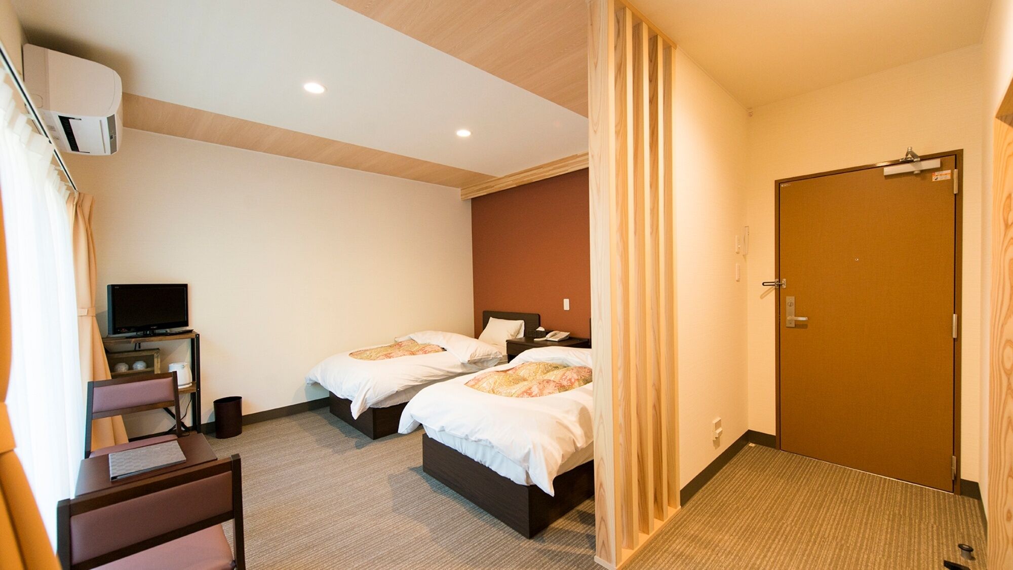 Ein Hotelzimmer mit zwei Betten, einem Schreibtisch mit Computer, einem Fernseher und einer Tür.