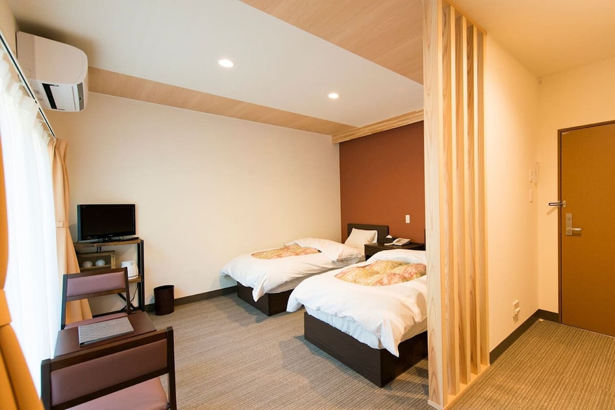Habitación de hotel con dos camas, un escritorio con computadora, televisor y una puerta.