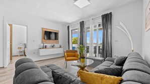 A modern living room with a grey sofa set, a yellow accent pillow, a glass coffee table, and a mounted TV. - Modern Family Villa Mia with Private Pool (Radeki Polje)