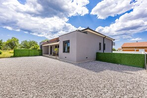 Une maison moderne avec une allée en gravier et une haie verdoyante.