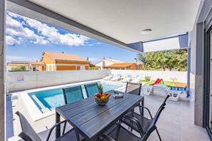 Un espace aménagé au bord de la piscine, avec une table, des chaises et un panier de fruits.