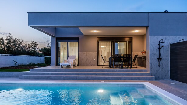 Una casa moderna con piscina, un patio con mobiliario exterior y un garaje.