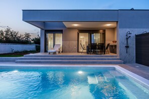 Ein modernes Haus mit Swimmingpool, einer Terrasse und Gartenmöbeln sowie einer Garage.