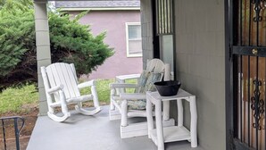 A covered porch with two rocking chairs and a small table, a black lantern on the wall, and a wooden door with a metal gate.