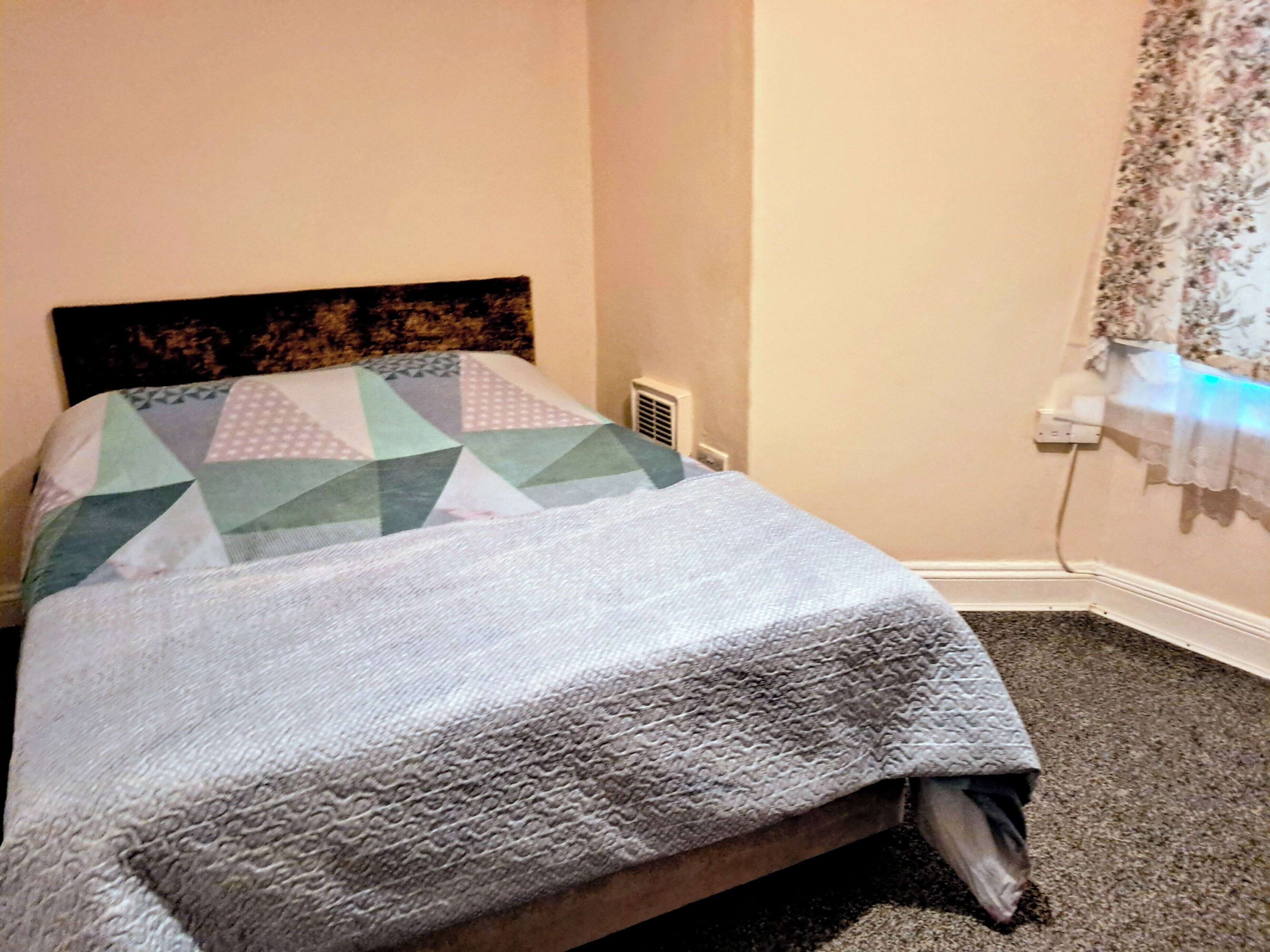 Uma cama com colcha de padrão geométrico e manta cinza texturizada.