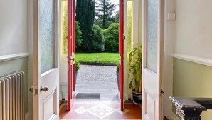 A doorway leading to a garden with a red door, a white radiator, and a black table with a decorative top.