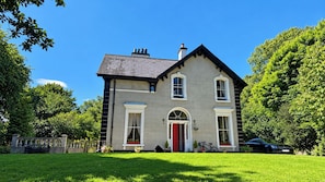 A two-story house with a red door, a balcony, and a car parked in front.