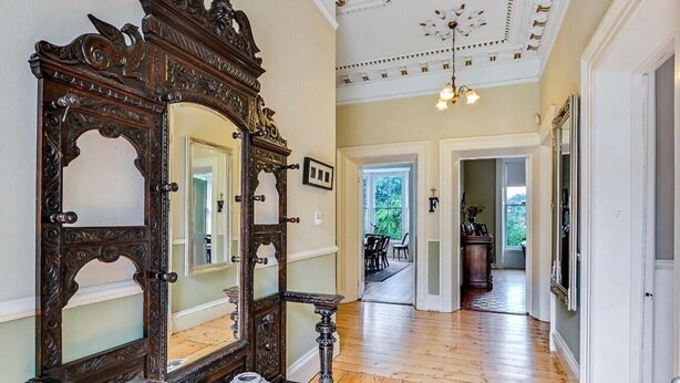 A hallway with wooden flooring, ornate mirrors, and a ceiling with decorative moldings.