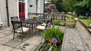 An outdoor patio with a table and chairs, surrounded by potted plants and flowers.