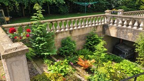 Un jardín con un muro de piedra, diversas plantas y una valla metálica.