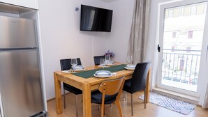 Un coin repas avec une table en bois, des chaises, un téléviseur à écran plat fixé au mur et une vue sur l’extérieur par une porte.