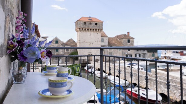 Un balcon avec une table dressée pour le thé, offrant une vue sur une tour historique et un port de plaisance.