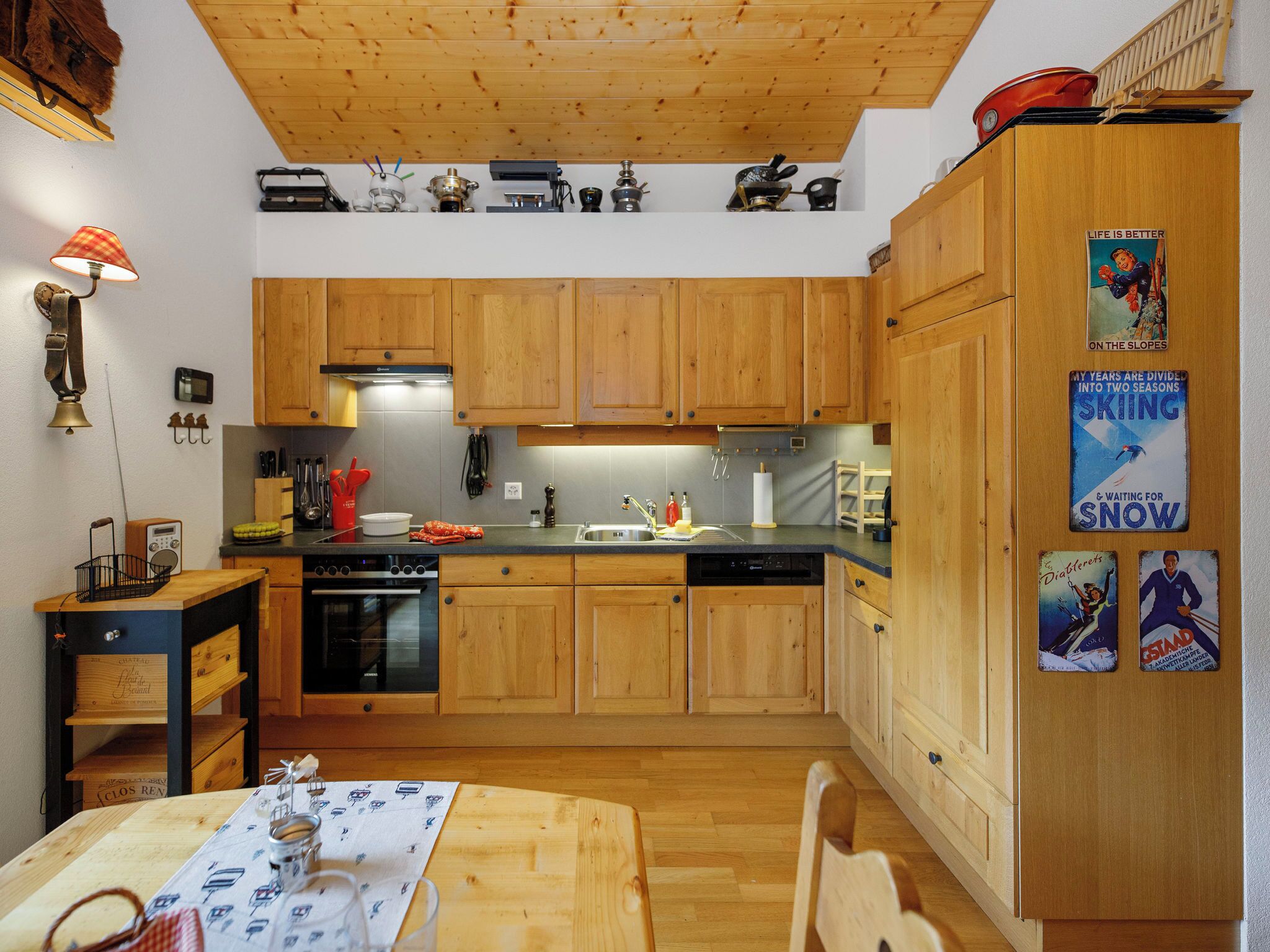 Une cuisine avec des armoires en bois, une cuisinière et un évier. On y trouve divers ustensiles et appareils de cuisine sur les plans de travail.