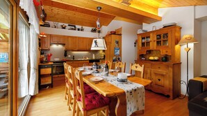 A wooden dining table set with plates, glasses, and a cake, surrounded by wooden chairs. - Mon Abri B by Interhome (Les Diablerets)