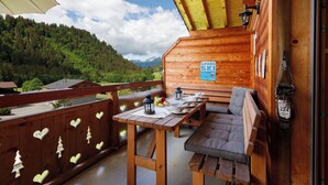 A wooden cabin with a balcony, a table with chairs, a sign reading 'APRES SKI Party Here Daily,' and a view of a forested mountain range. - Mon Abri B by Interhome (Les Diablerets)