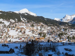 Un village enneigé, avec ses maisons traditionnelles en bois, un télésiège et des montagnes en arrière-plan.