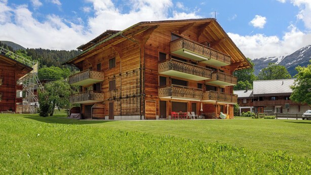 A multi-story wooden building with balconies, a grassy lawn, and mountains in the background. - Mon Abri B by Interhome (Les Diablerets)