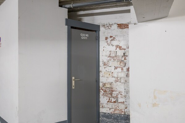 Une porte dotée d’un cadre en métal et d’une poignée en laiton, qui donne sur une pièce dont un des murs est en briques peintes en blanc.