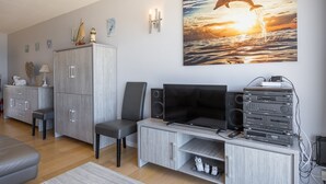 Un salon moderne doté d’un téléviseur à écran plat, d’un système audio et d’un grand tableau représentant un dauphin sautant hors de l’eau, accroché au mur.
