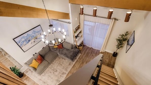 A modern living room with a gray sofa, a wooden staircase, and a chandelier. - Modern condo with heated pool and hot tub (Mammoth Lakes)