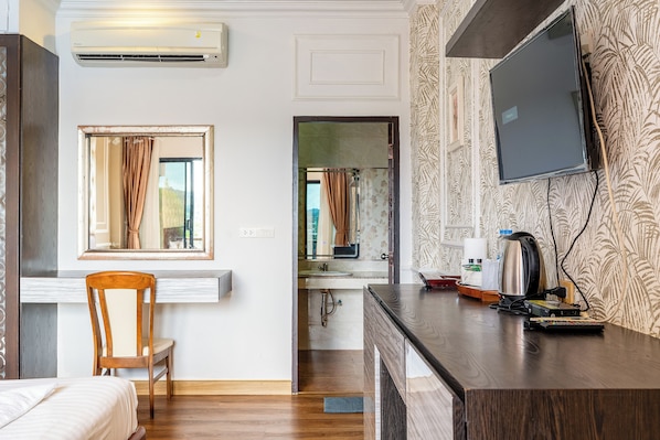 A hotel room with a wooden bed, a desk with a kettle, a television, and a bathroom visible through an open door. - Samprasob Resort (Sangkhla Buri)