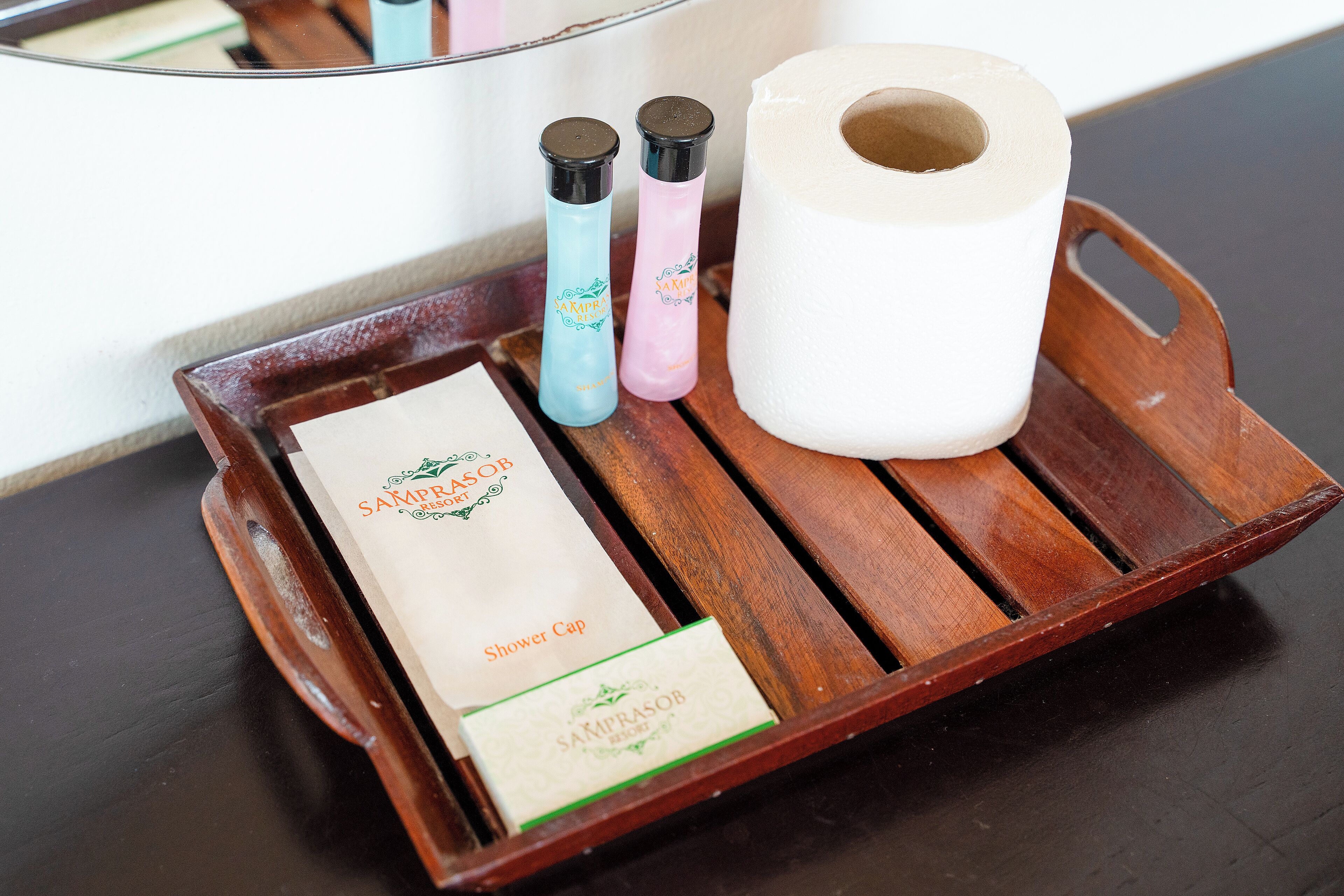 A wooden tray with a shower cap, two bottles, and a roll of toilet paper.