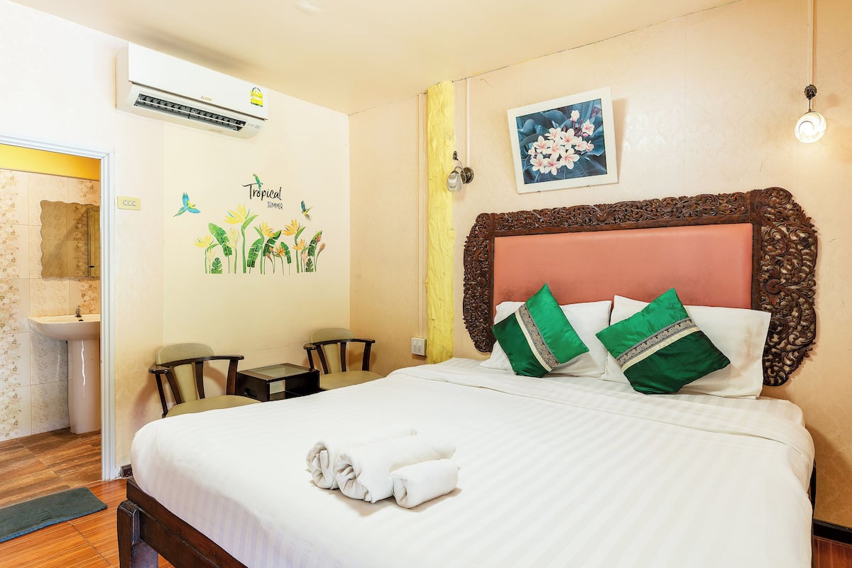 A neatly made bed with green and white pillows, a wooden headboard, and a tropical-themed wall decal.
