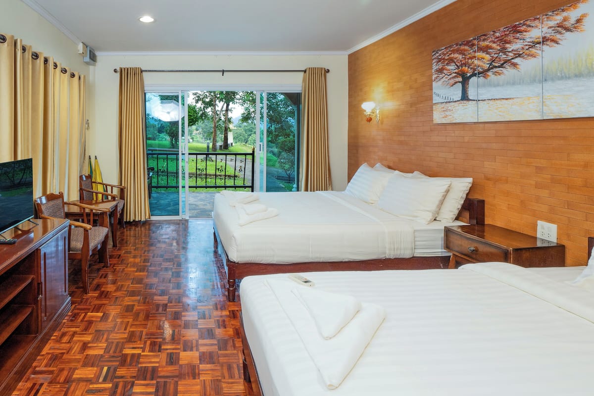 A hotel room with two beds, a TV, a desk with chairs, and a painting on the wall.