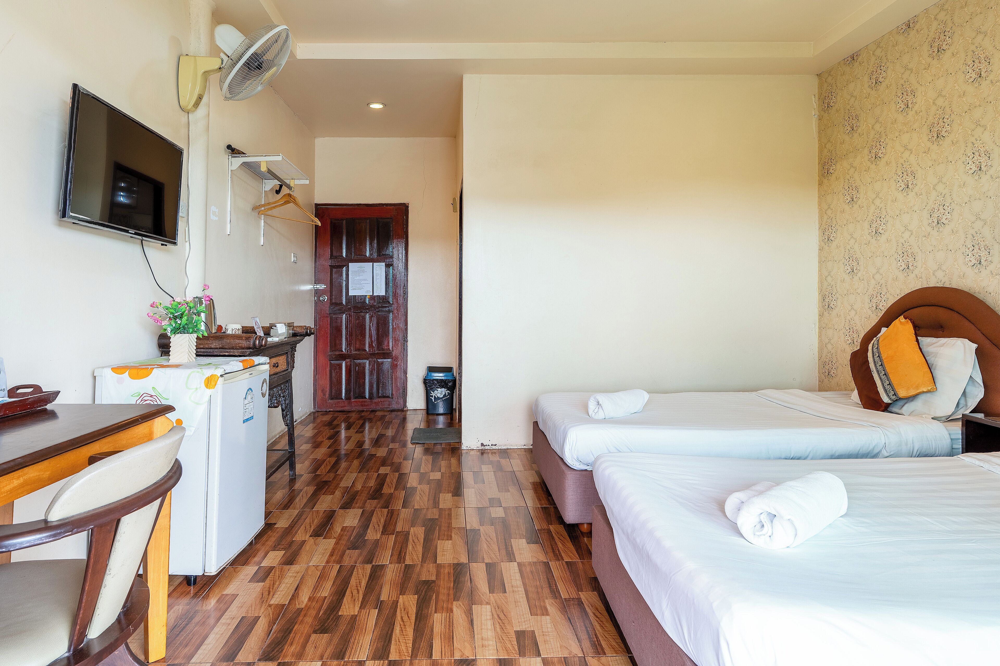 A hotel room with two beds, a desk with a chair, a television, and a refrigerator.