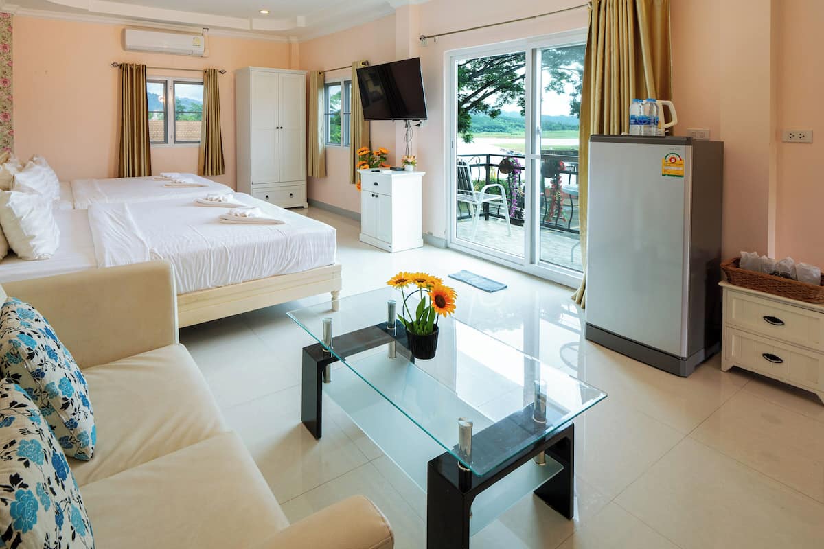 A hotel room with a bed, a sofa, a glass coffee table, a TV, a refrigerator, and a balcony with a view.