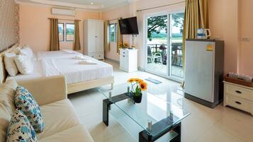 Habitación de hotel con cama, sofá, una mesa de centro de vidrio, televisor, refrigerador y balcón con vistas.