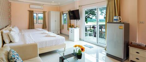 A hotel room with a bed, a sofa, a glass coffee table, a TV, a refrigerator, and a balcony with a view.