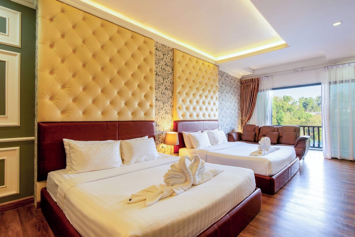 A hotel room with two beds, a sofa, and a balcony with curtains.