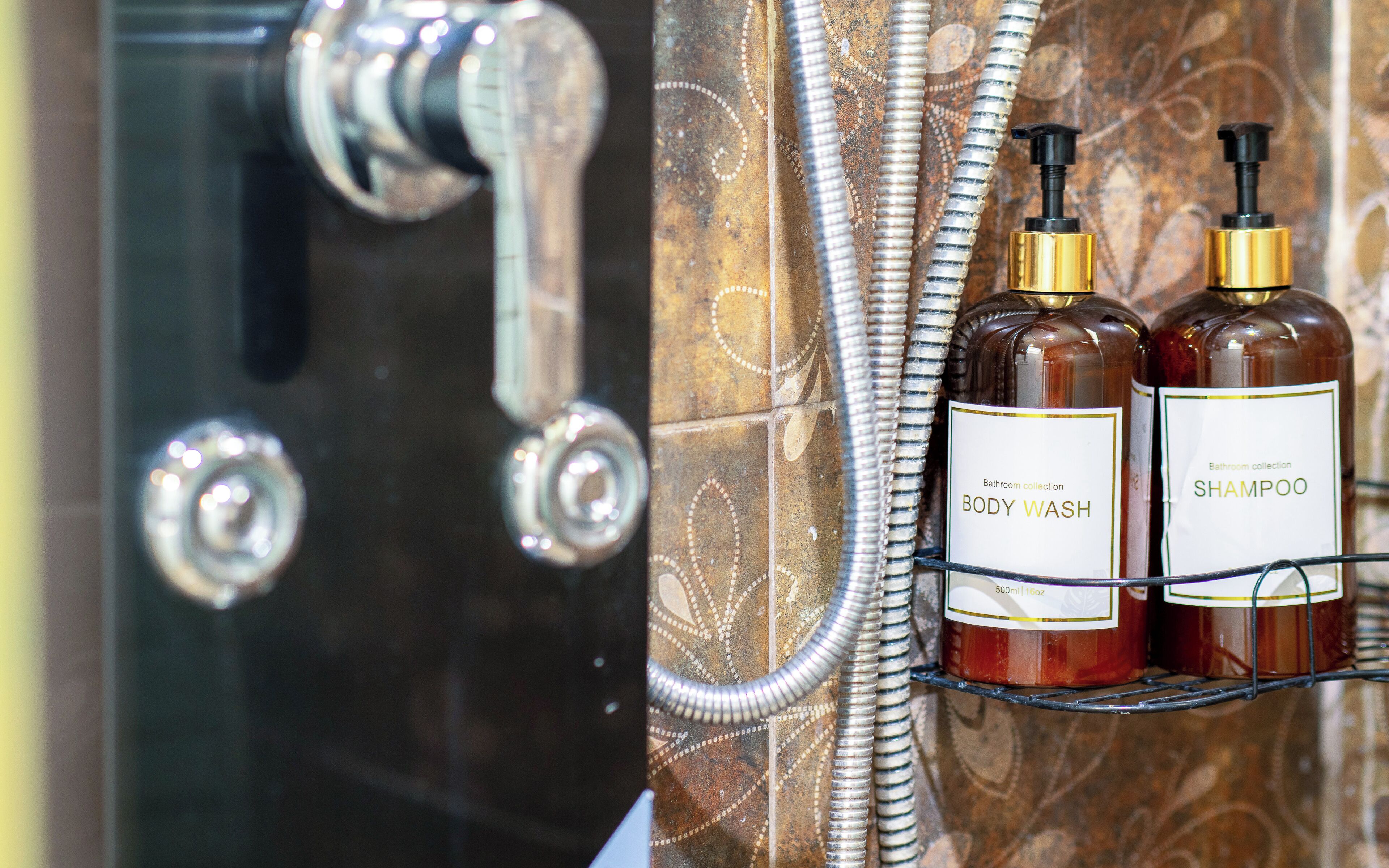 A bathroom with a shower, a faucet, and two bottles of shampoo on a rack.