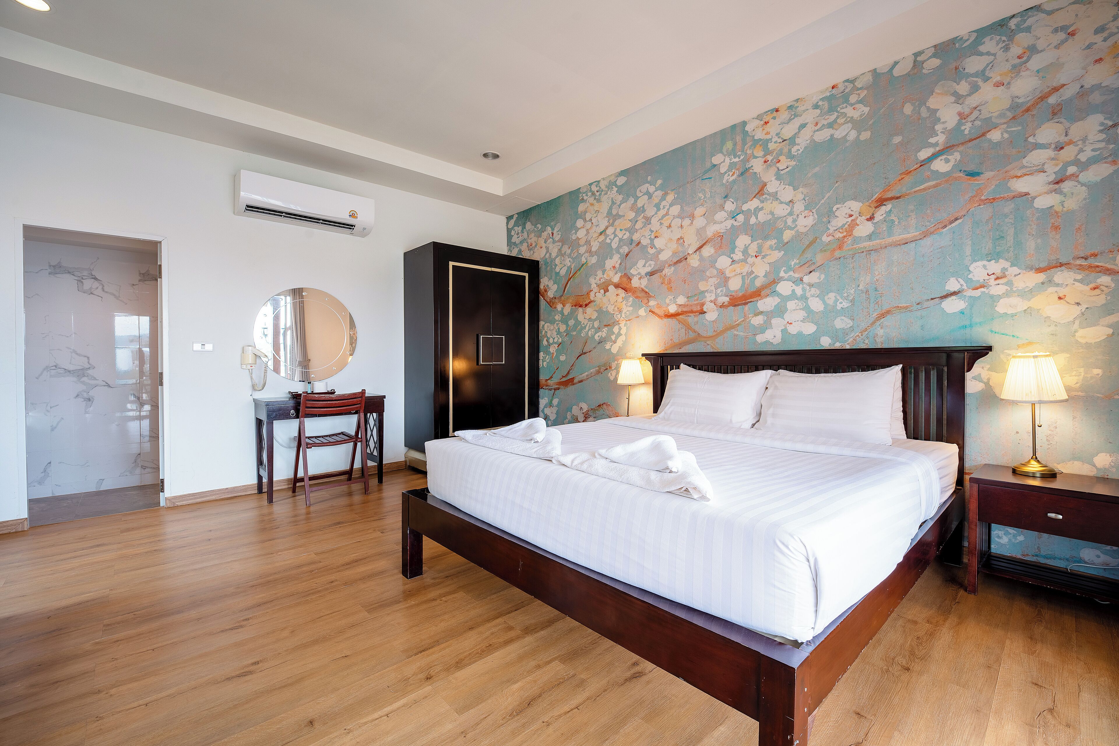 A bedroom with a wooden bed, a large wall mural, a desk with a chair, and a wardrobe.
