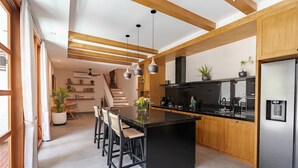 A modern kitchen with a central island, wooden beams, pendant lighting, and a stainless steel refrigerator.