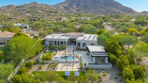 A modern house with a swimming pool, surrounded by greenery and mountains.