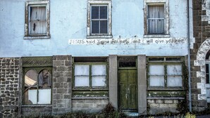 A building with three windows, a green door, and a sign with a biblical quote.