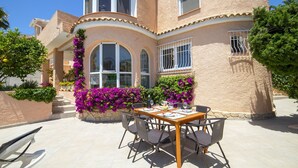 A patio with a table and chairs, surrounded by vibrant flowers and a building with arched windows and a stucco exterior. - Santa Barbara by Interhome (Calpe/Calp)