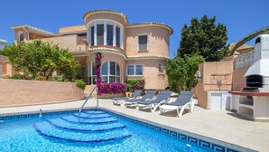 A pool area with a clear blue pool, lounge chairs, and a building with a curved facade. - Santa Barbara by Interhome (Calpe/Calp)