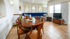 A dining area with a wooden table and chairs, a blue sofa, and a television in a corner. - Santa Barbara by Interhome (Calpe/Calp)