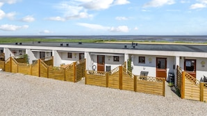 A row of white buildings with numbered doors, a gravel area in the foreground, and a view of the sea and sky in the background. - "Kjera" - 2.4km from the sea by Interhome (Rømø)
