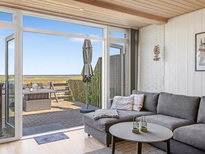 A modern living room with a grey sofa, a round coffee table, and a glass door leading to an outdoor patio.