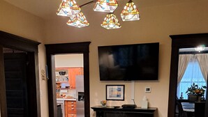 Una sala de estar con chimenea, un televisor montado en la pared y un comedor visible a través de un vano abierto.
